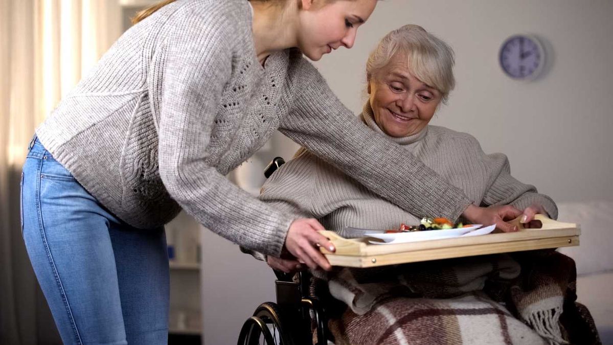 Asistentka podává seniorce jídlo